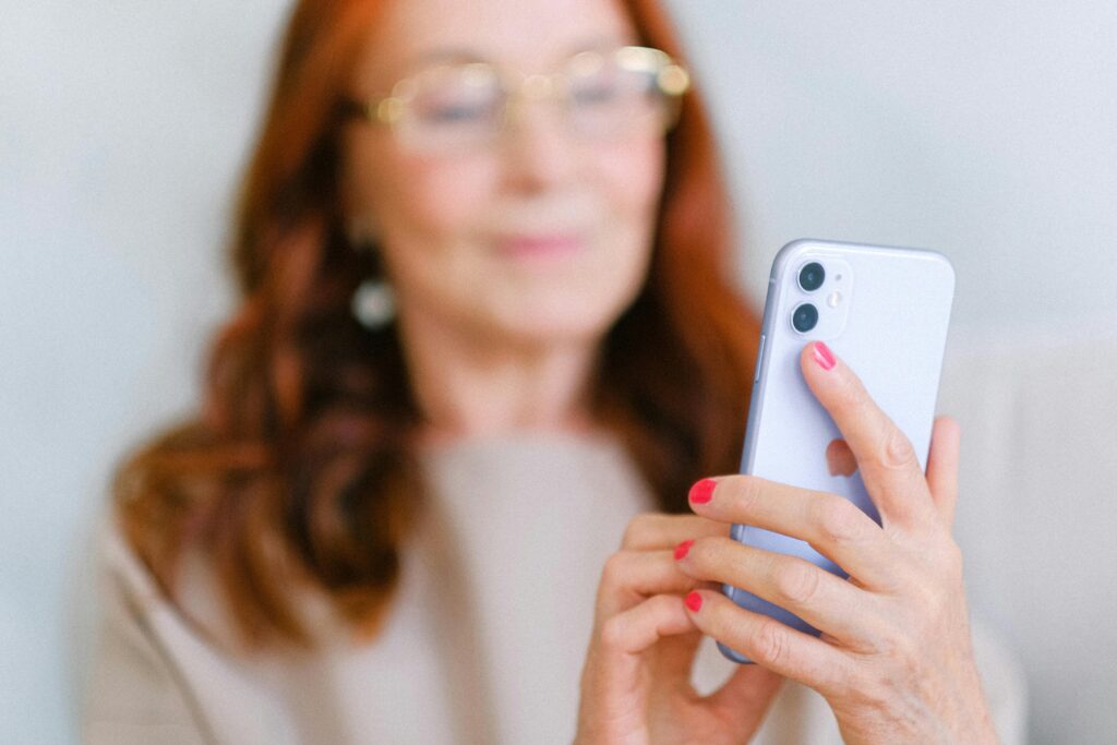 uma idosa de pele branca e cabelos ruivos mexe em um celular de cor roxa