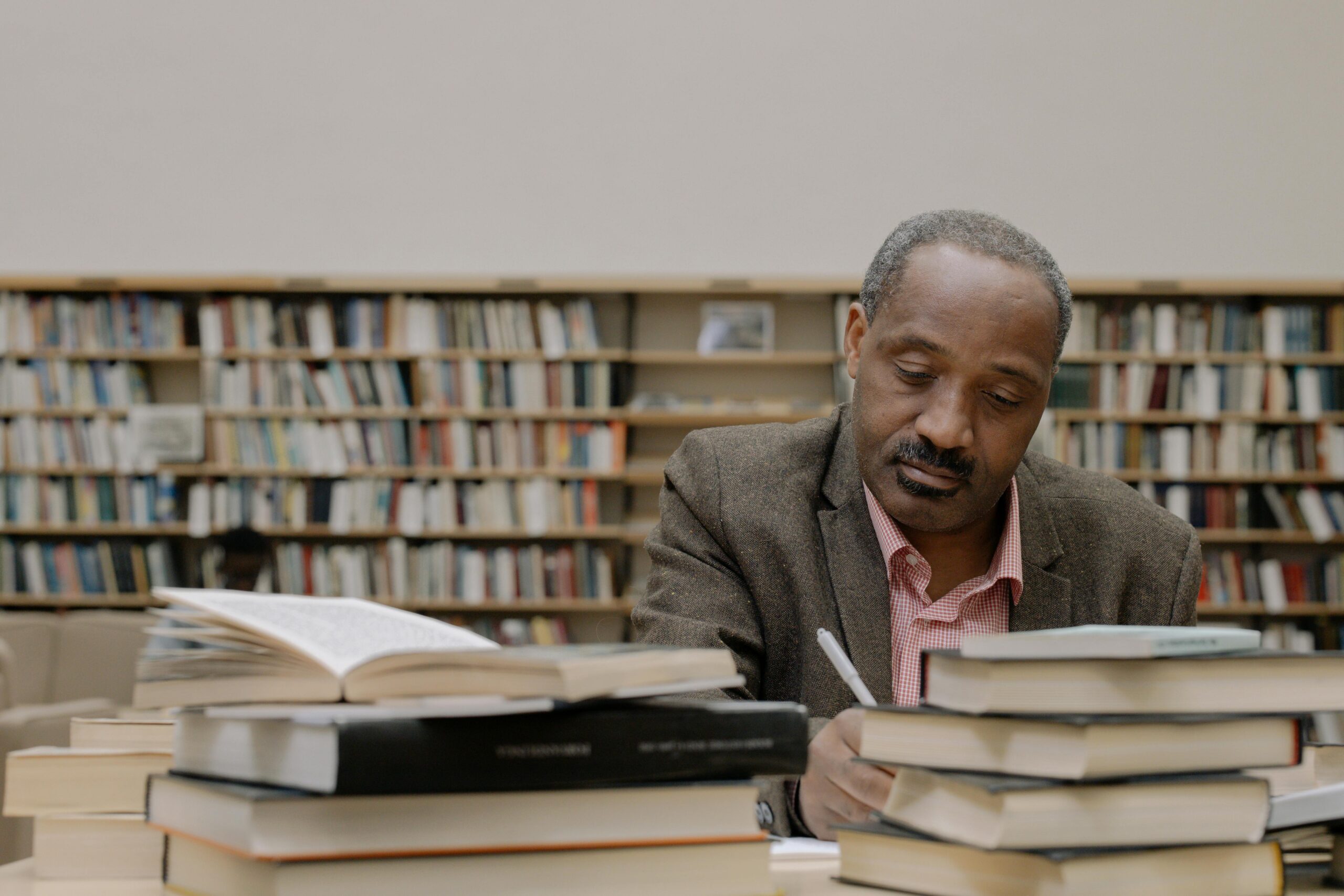 um senhor pele negra lê uma pilha de livros em uma mesa